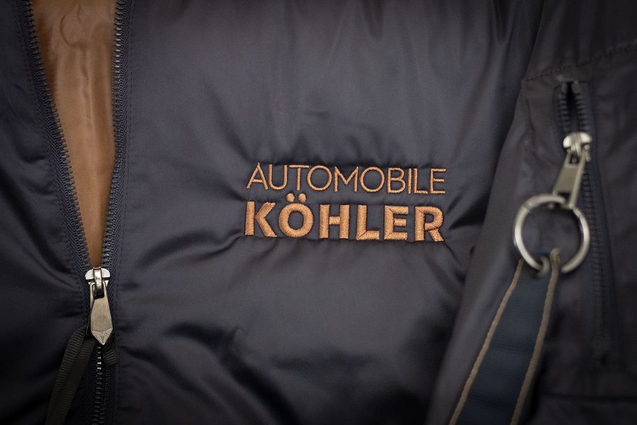 Dunkelblaue Steppjacke mit kupferfarben gesticktem Logo Automobile Köhler