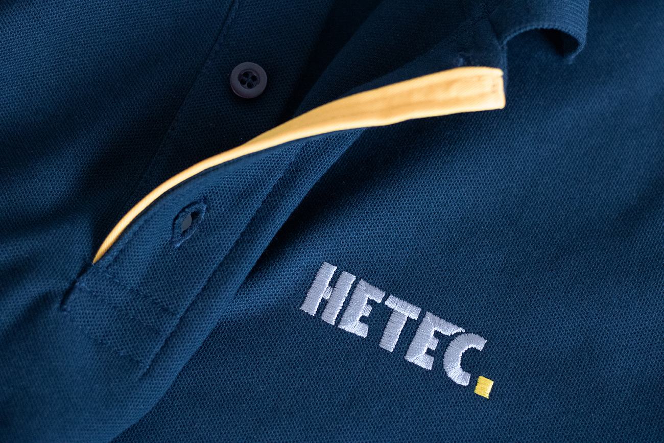 Dasselbe dunkelblaue Poloshirt mit gesticktem HETEC-Logo auf der Brust